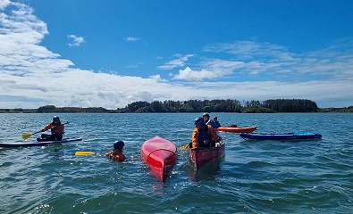 A canoe and paddler are being rescued by two other canoe paddlers on a Paddlesport Touring Leader Assessment whilst a kayaker and paddleboard look on.